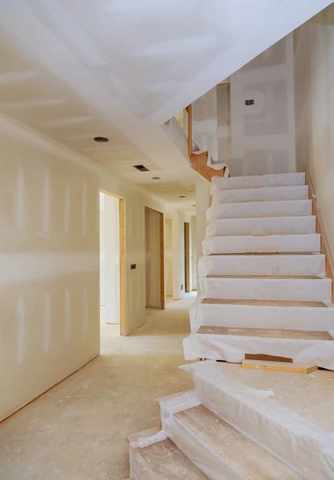 Intérieur de maison en cours de finition avec escalier en béton brut et murs en plaques de plâtre non peints