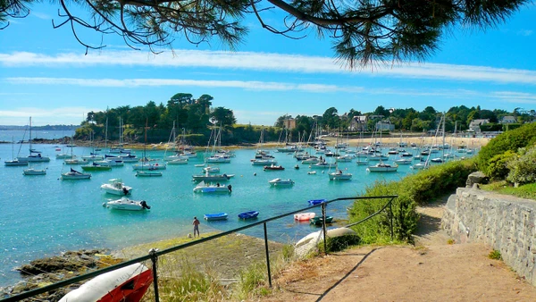Photographie en couleur d'une vue caractéristique de Saint-Briac-sur-Mer en Bretagne : paysage côtier avec plage de sable, falaises côtières et rochers granitiques typiques de la Côte d'Émeraude. La scène capture l'essence bretonne du littoral nord avec ses formations géologiques distinctives, prise de jour avec une bonne luminosité naturelle. Sans texte, logo ou filigrane.